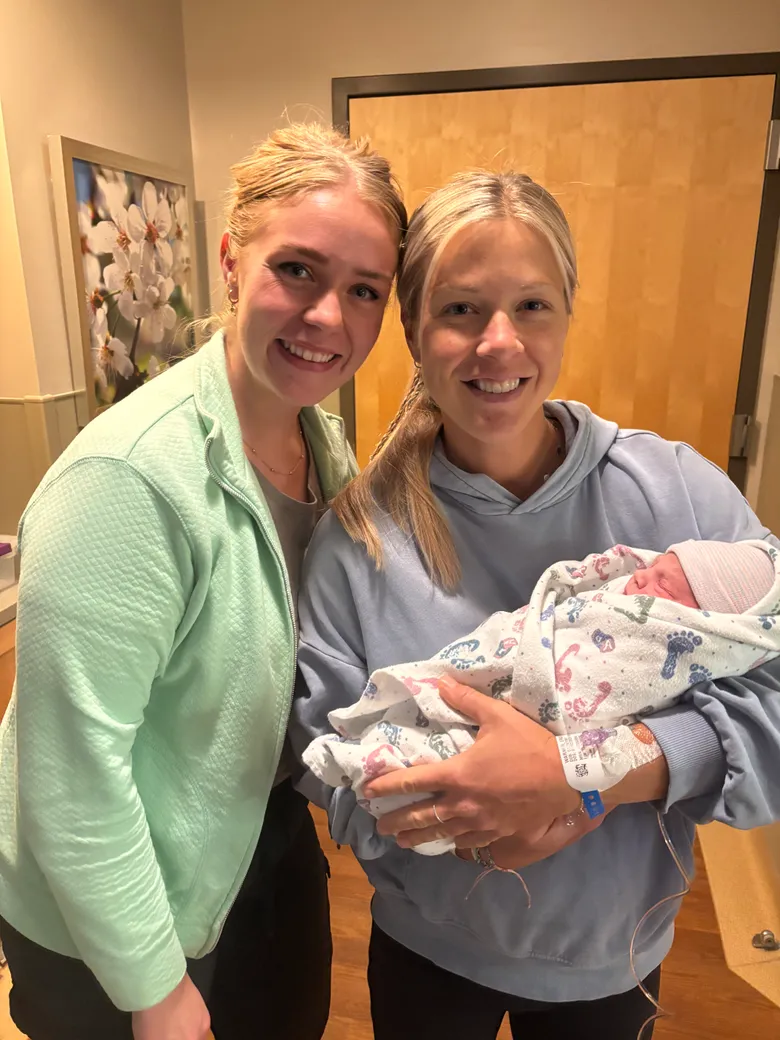 A postpartum doula holding a newborn wrapped in a blanket